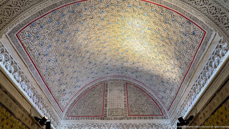 Large polygonal palace vault covered in dense blue-and-gold arabesque patterns, framed by white carved-plaster borders and red edging.