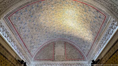 Large polygonal palace vault covered in dense blue-and-gold arabesque patterns, framed by white carved-plaster borders and red edging.