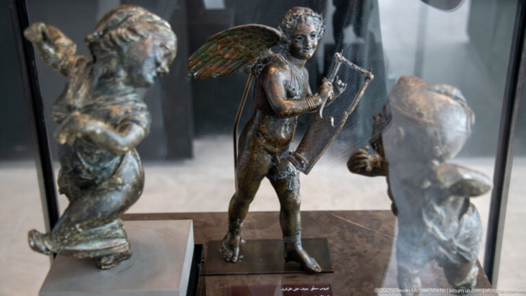 Winged bronze Eros from the Mahdia shipwreck standing with a kithara held upright against his body.