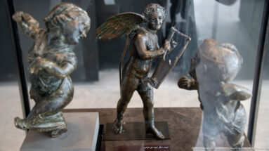 Winged bronze Eros from the Mahdia shipwreck standing with a kithara held upright against his body.
