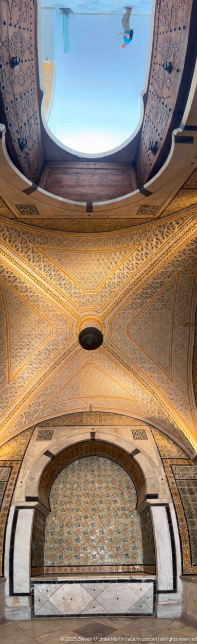 Wide-angle view of a marble-framed tiled alcove beneath an ornate vaulted ceiling with dark flanking tile panels.