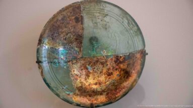 Large shallow green-blue glass dish mounted vertically, with brown and violet iridescent weathering and faint linear decoration.
