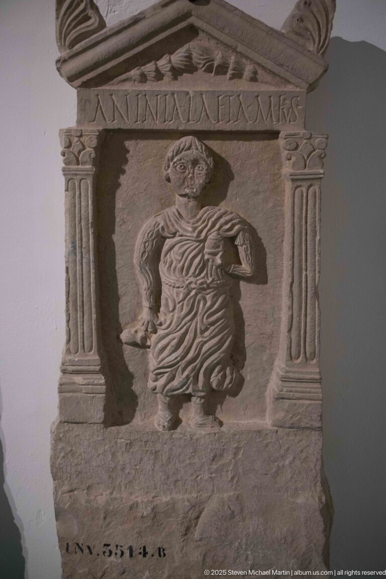 Inscribed stone stele with a standing draped woman framed by fluted columns and a triangular pediment.
