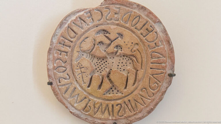 Circular carved stone disk with a mounted rider in the center and a continuous inscription around the outer border.