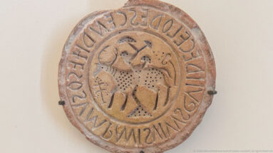 Circular carved stone disk with a mounted rider in the center and a continuous inscription around the outer border.