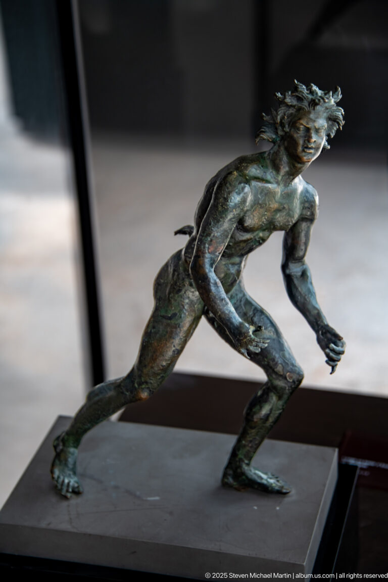 Bronze satyr from the Mahdia shipwreck lunging forward with bent knees, outstretched arms, wild hair, and an aggressive expression.