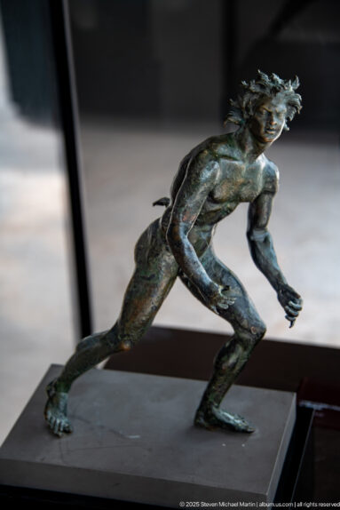 Bronze satyr from the Mahdia shipwreck lunging forward with bent knees, outstretched arms, wild hair, and an aggressive expression.