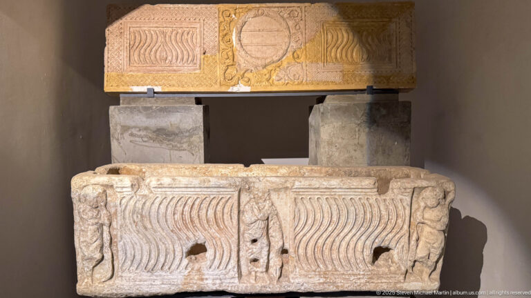 Two stacked carved stone blocks with repeated vertical wave patterns below and a large circular medallion on the upper block.