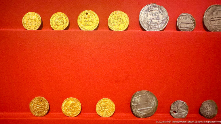 Two rows of gold, silver, and bronze coins and stamped pieces displayed on red felt, including inscribed and portrait types.