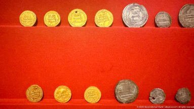 Two rows of gold, silver, and bronze coins and stamped pieces displayed on red felt, including inscribed and portrait types.