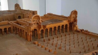 Wooden architectural model of a rectangular arcaded courtyard complex with towers, gateways, and many small columns or posts.