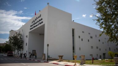 Modern white Bardo Museum entrance with multilingual signage, small square windows, and stone antiquities lining the approach.