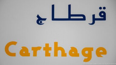 White gallery wall with the word Carthage in ochre beneath large dark blue Arabic lettering.