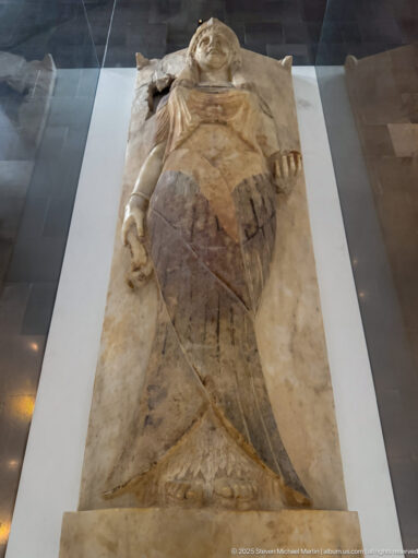 Full-length recumbent female figure carved on a rectangular stone funerary slab, viewed from above.