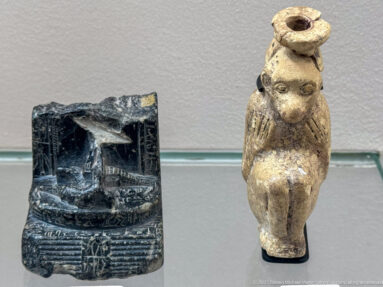 Two small ancient objects: a dark rectangular relief piece and a pale frontal figurine with a cylindrical top opening.