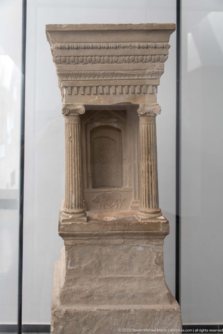 Small carved stone stele shaped like an architectural façade with side columns, recessed niche, and layered entablature.