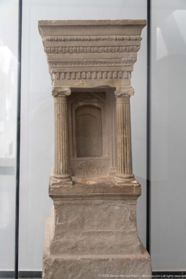 Small carved stone stele shaped like an architectural façade with side columns, recessed niche, and layered entablature.