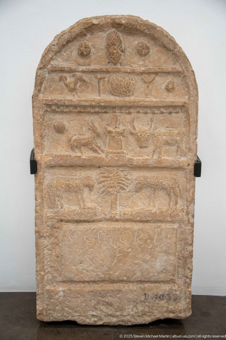 Rounded-top stone stele divided into horizontal registers with circular symbols and shallow animal reliefs.