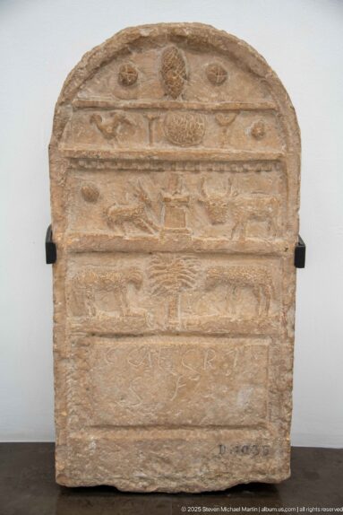 Rounded-top stone stele divided into horizontal registers with circular symbols and shallow animal reliefs.
