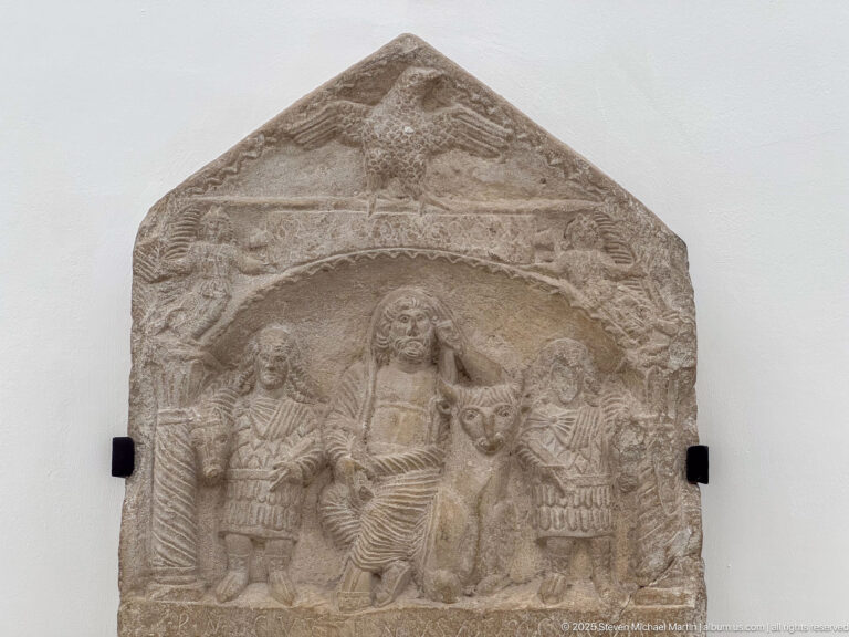 Gabled stone relief with a central standing female figure, smaller attendants, animals, and dense carved ornament.