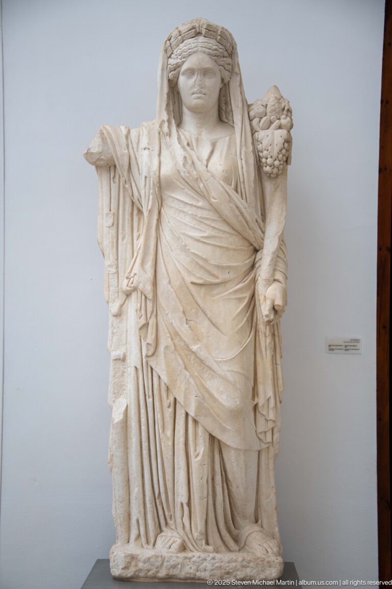 Large stone statue of a draped woman holding a cornucopia beside her shoulder.