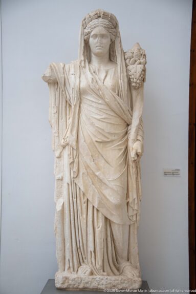 Large stone statue of a draped woman holding a cornucopia beside her shoulder.