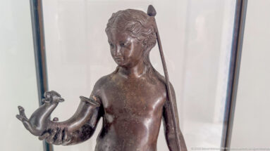 Bronze female statuette with wavy hair, a long support behind her shoulder, and a small animal resting on one hand.