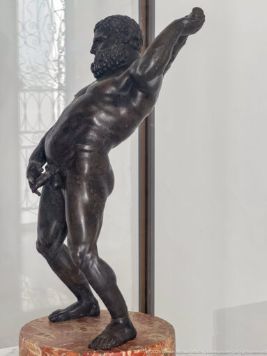 Nude bronze male figure crouching and leaning forward with both arms extended in a dynamic athletic pose.