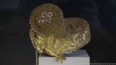Gold-embroidered slipper with sequins, raised floral motifs, and a large decorative rosette near the opening.