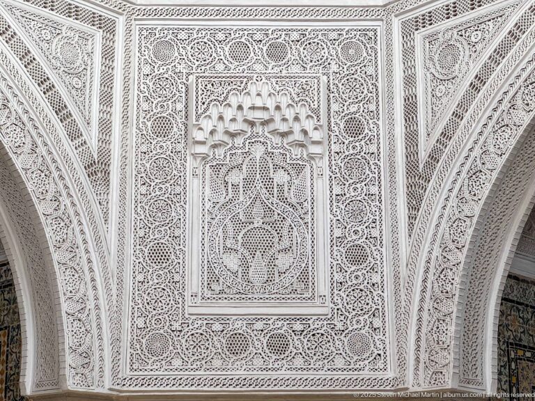 White carved-plaster panel filled with geometric interlace, rosettes, and a small recessed muqarnas-like central niche.