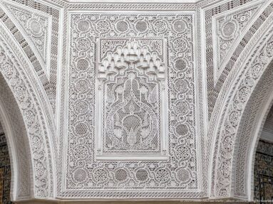 White carved-plaster panel filled with geometric interlace, rosettes, and a small recessed muqarnas-like central niche.