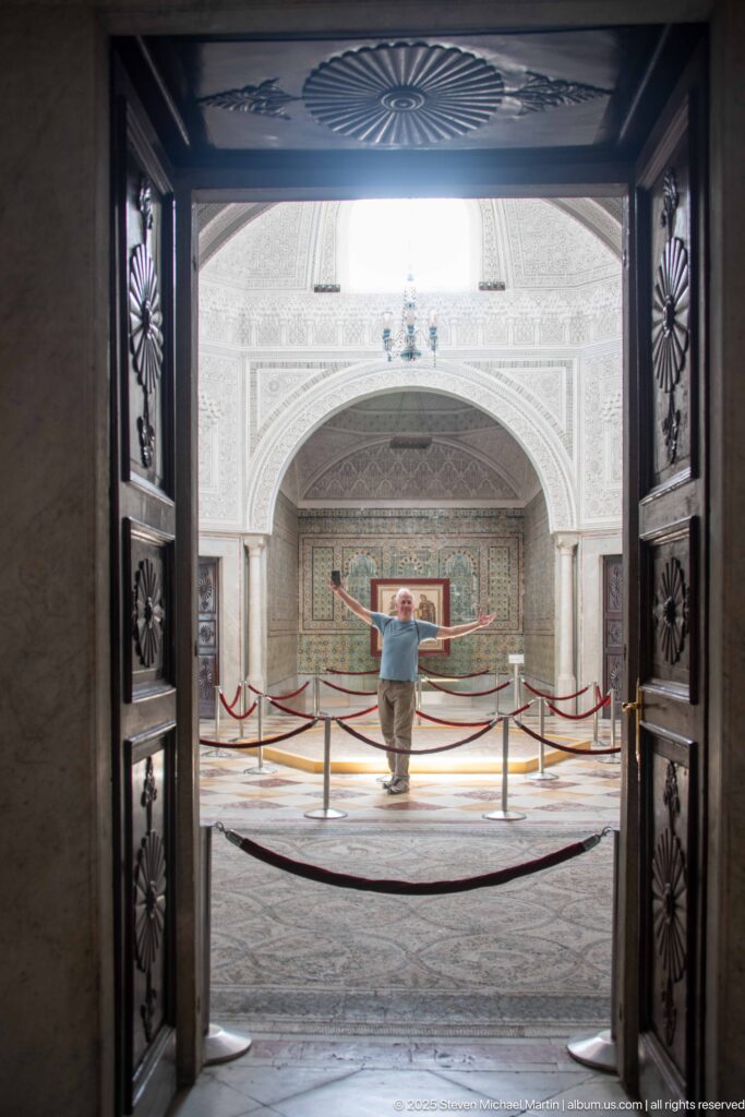 Open carved wooden doors framing a visitor and mosaic display in a bright vaulted gallery beyond.