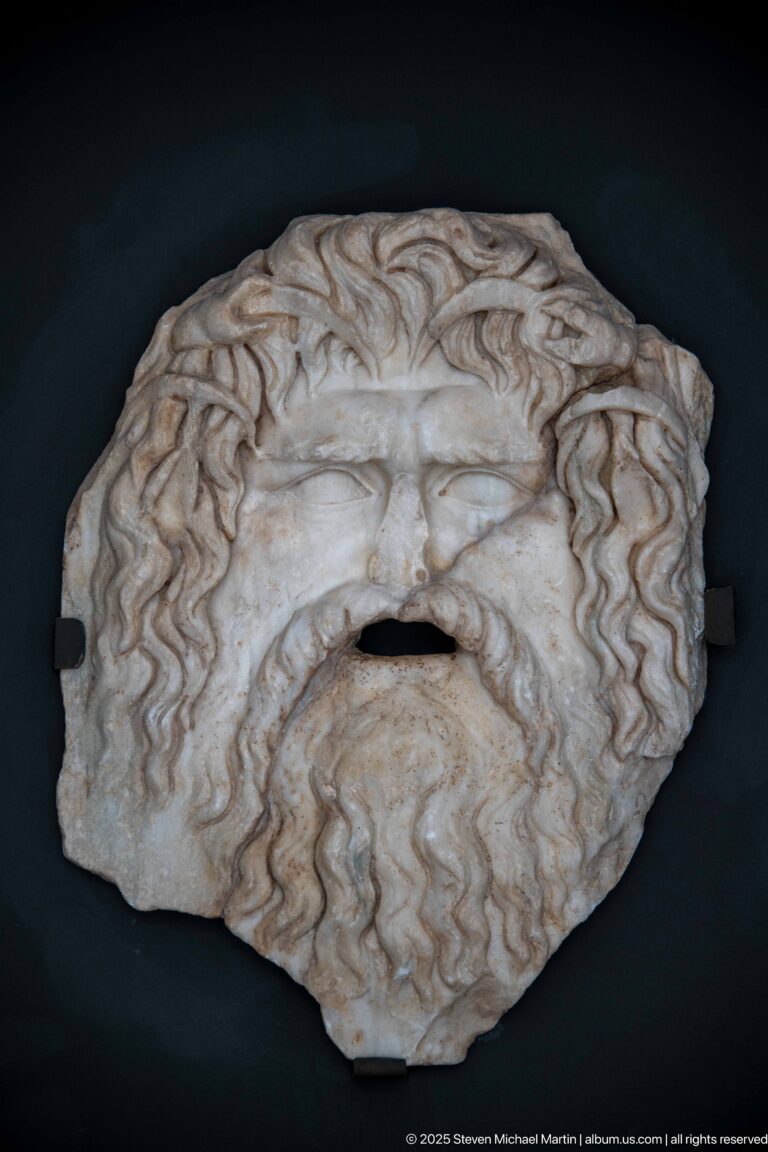 Marble face or mask fragment surrounded by deeply carved wavy hair, with an opening at the mouth.