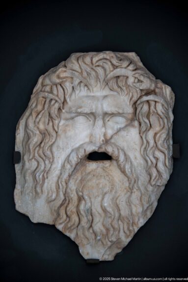 Marble face or mask fragment surrounded by deeply carved wavy hair, with an opening at the mouth.