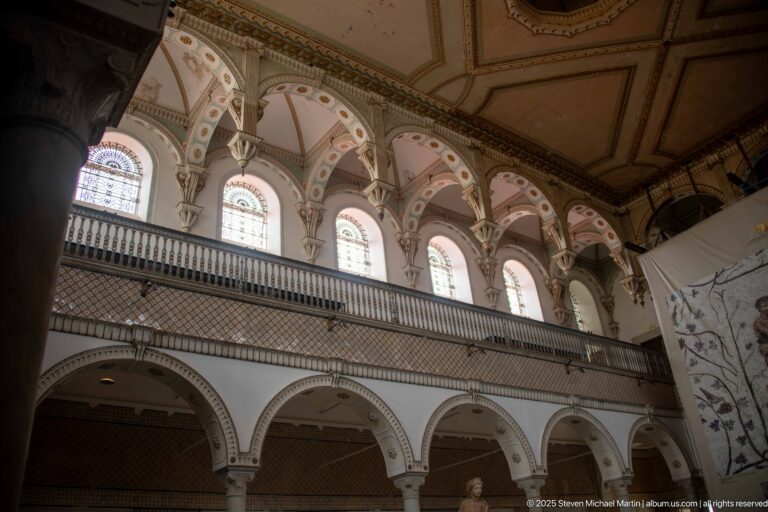 Upper gallery arcade with arched windows, decorative spandrels, lattice balustrade, and columns below.