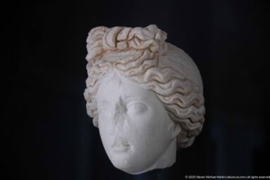 Marble female head with wavy swept-back hair, smooth idealized features, and a small central diadem.