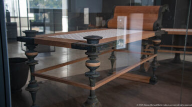 Reconstructed rectangular table with turned legs and a couch or bed displayed behind glass.