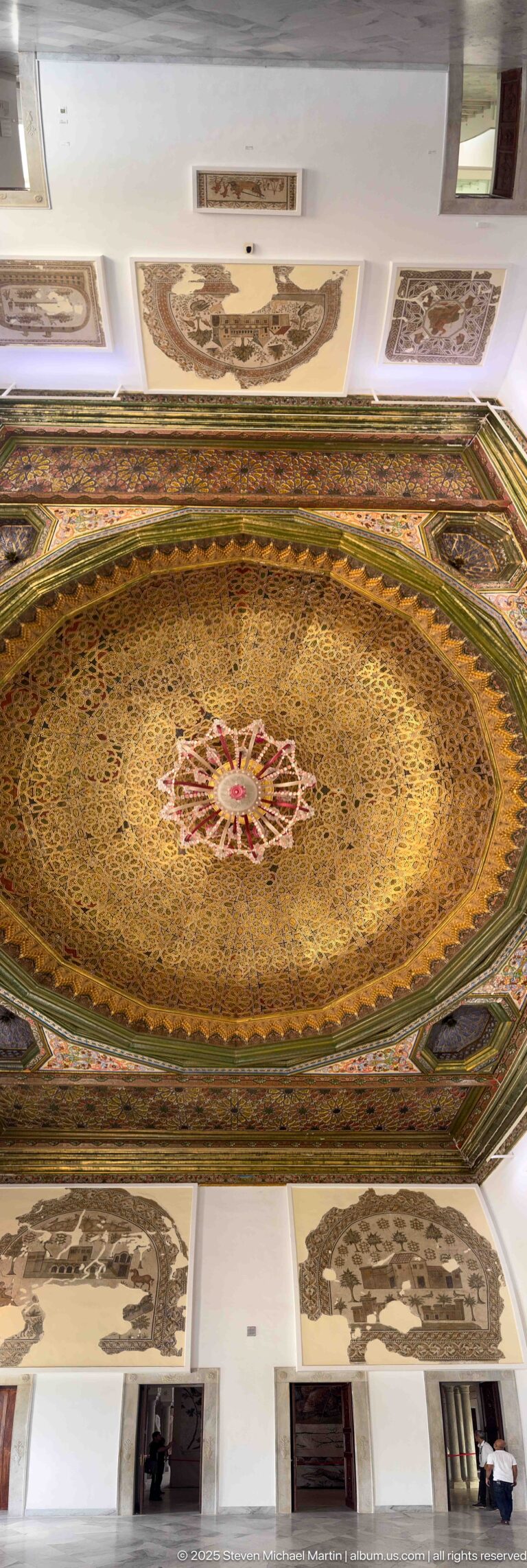 Oblique wide view of the ornate octagonal ceiling above white gallery walls hung with mosaics.