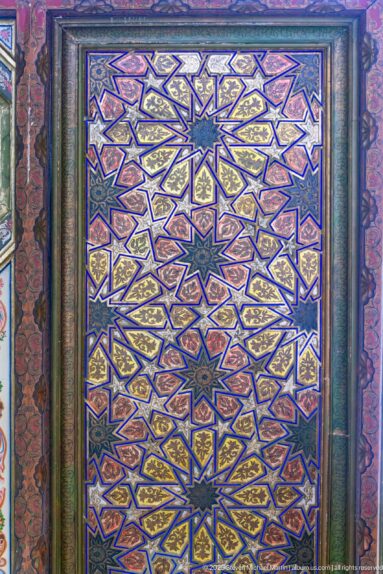 Polychrome wooden panel with interlocking blue, red, and gold star polygons arranged in a dense geometric pattern.