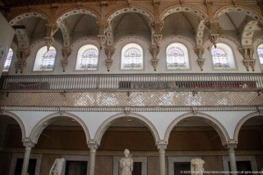 Upper Bardo Museum gallery with five arched windows, ornate surrounds, balustrade, and the tops of lower arches and statues.