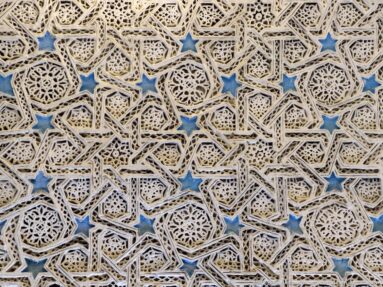 Close view of cream-colored openwork plaster with interlaced geometric stars, rosettes, pierced latticework, and blue-painted accents.