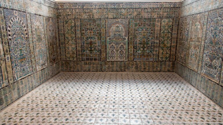 Symmetrical tiled chamber with multicolored wall panels, stylized niches, floral decoration, and a patterned ceramic floor.