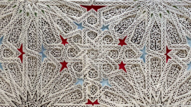 Cream openwork plaster lattice with interlaced stars, pierced arabesque carving, and small red and blue painted recesses.