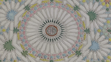 Large radial ceiling rosette with narrow white segments, a multicolored geometric border, and surrounding green and blue star motifs.