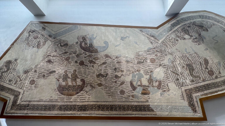 Large Roman maritime mosaic with ships, people, coastal buildings, fish, and sea creatures spread across an irregular field.
