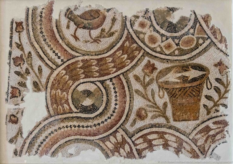 Roman mosaic fragment with central decorated vessel, small birds, leafy sprigs, and curling geometric bands.