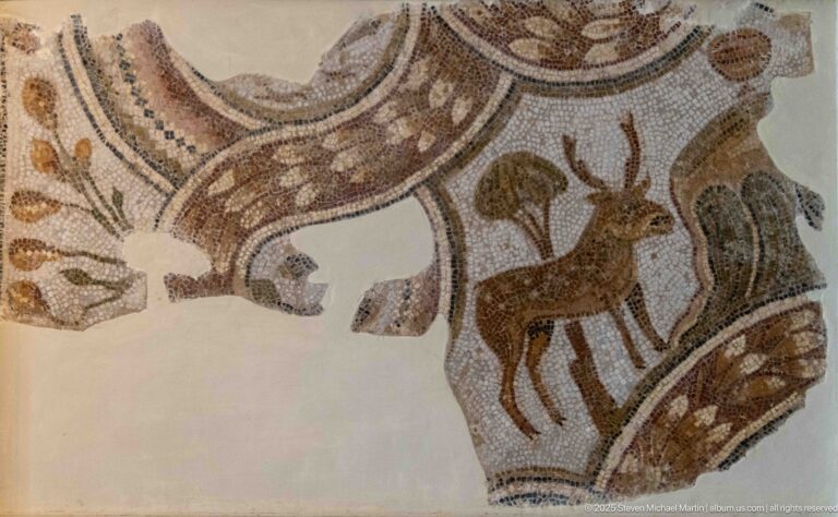 Slender horned antelope or gazelle standing inside a curved geometric mosaic compartment with plant motifs.
