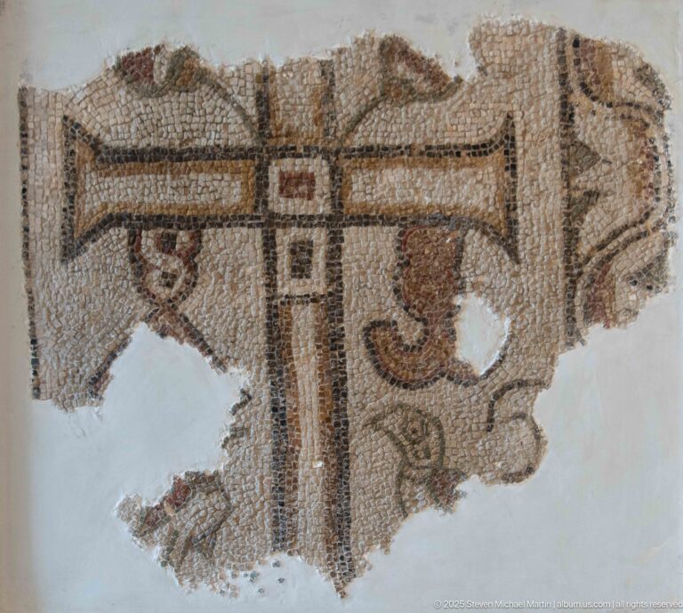 Fragmentary Christian mosaic with a large outlined cross and small flanking motifs, surrounded by extensive losses.
