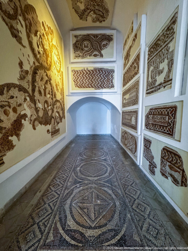 Narrow Bardo Museum gallery with geometric floor mosaics and Christian, inscribed, animal, and decorative wall mosaics.