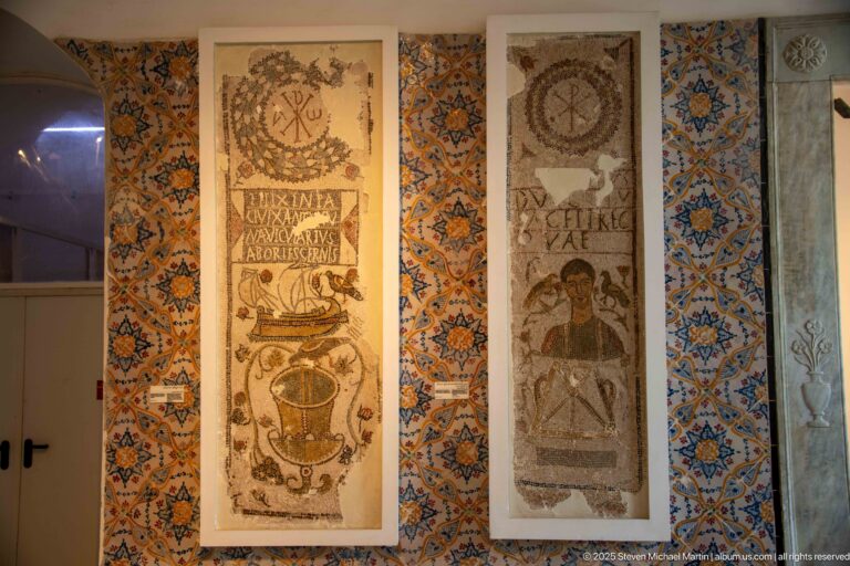 Two tall inscribed Christian mosaics with figures and circular motifs mounted against colorful patterned wall tiles.
